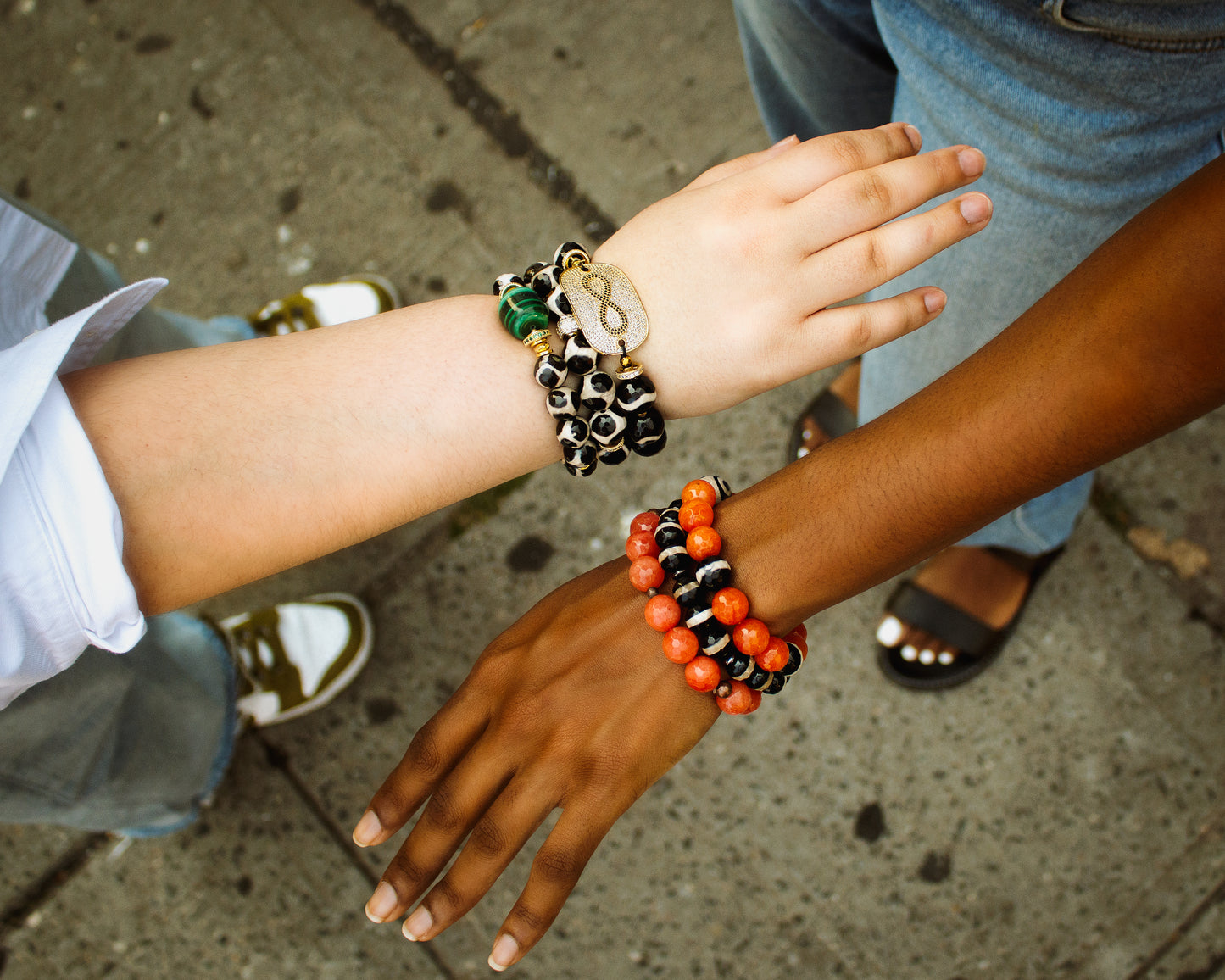 Two people wearing colorful beaded bracelets on a sidewalk.
