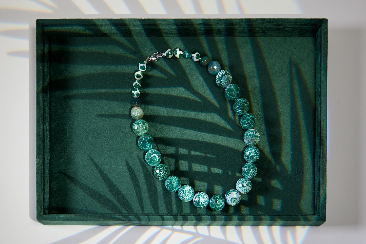 Green beaded bracelet on a dark green tray with leaf shadows