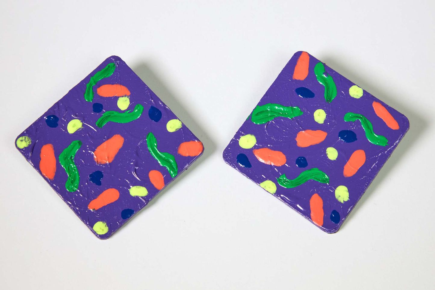 Two purple square earrings with colorful abstract designs on a white background