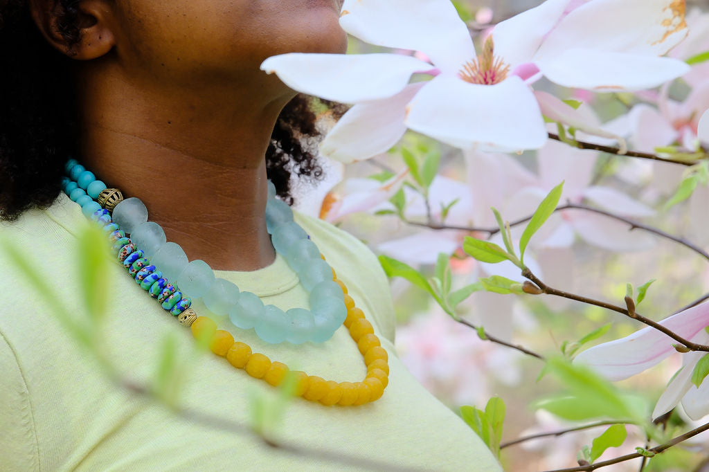 Person wearing a colorful beaded necklace with a blurred background of flowers