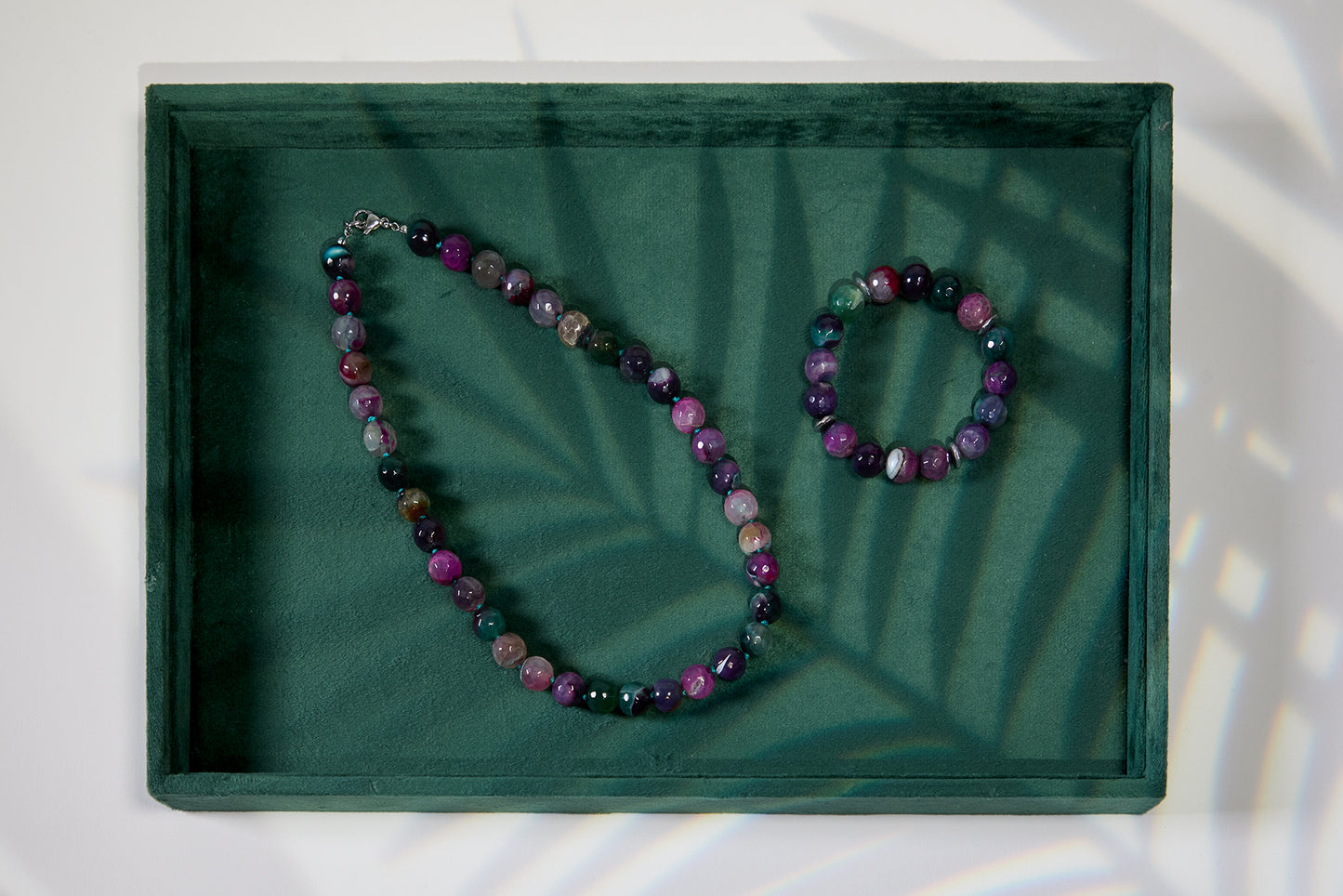 Gemstone necklace and bracelet set on a green tray with leaf shadows