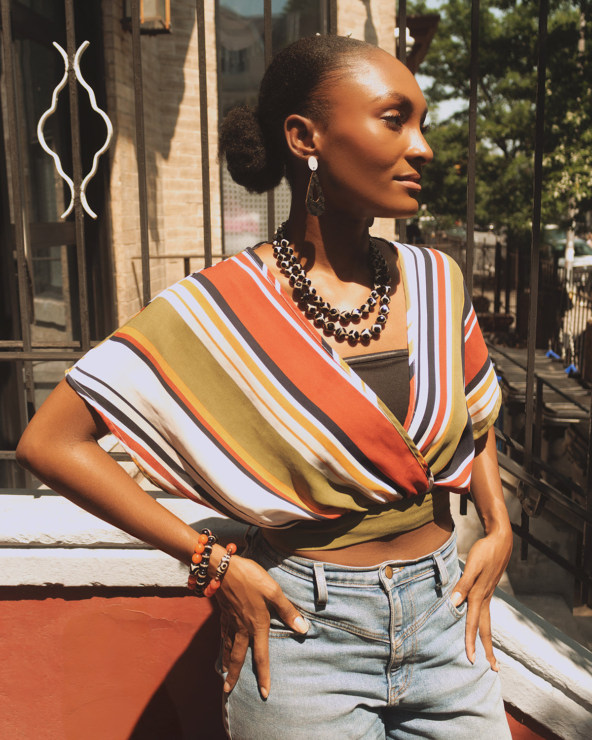 Woman wearing a colorful striped top and jeans outdoors.