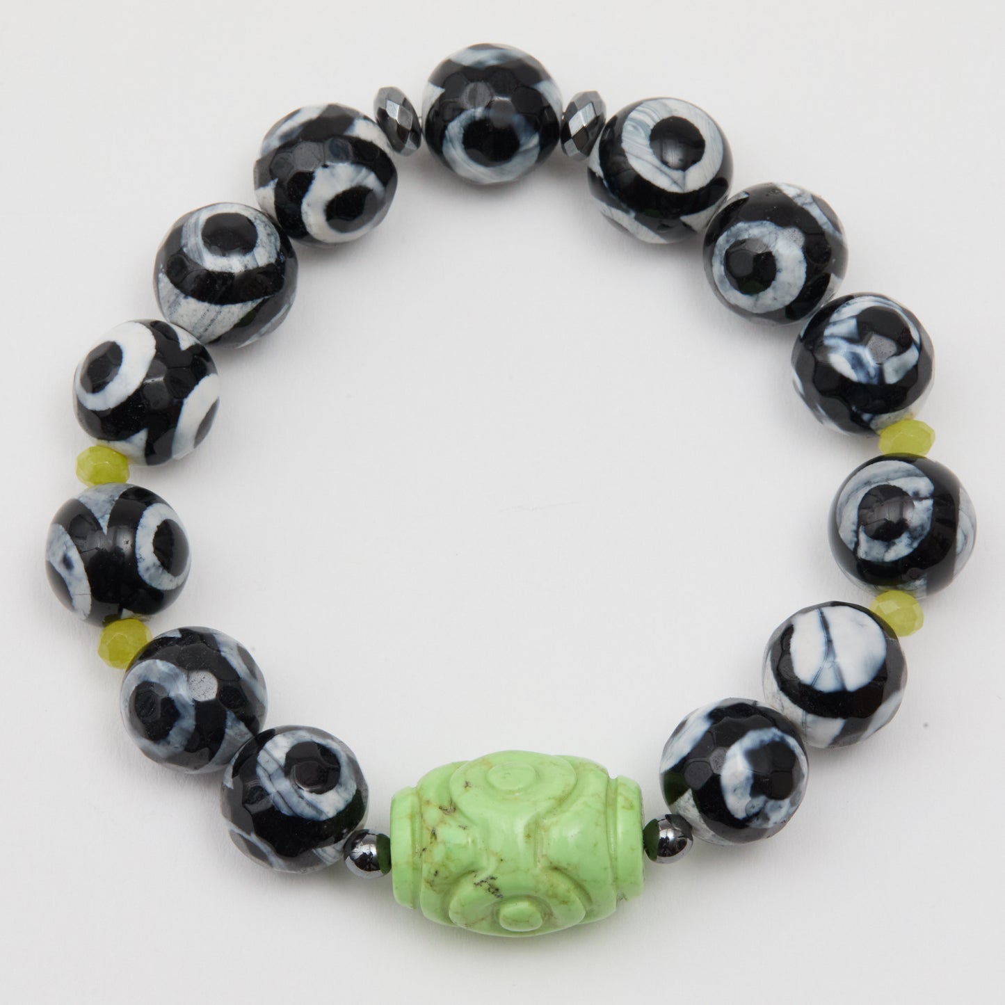 Black and white beaded bracelet with a green carved bead on a white background