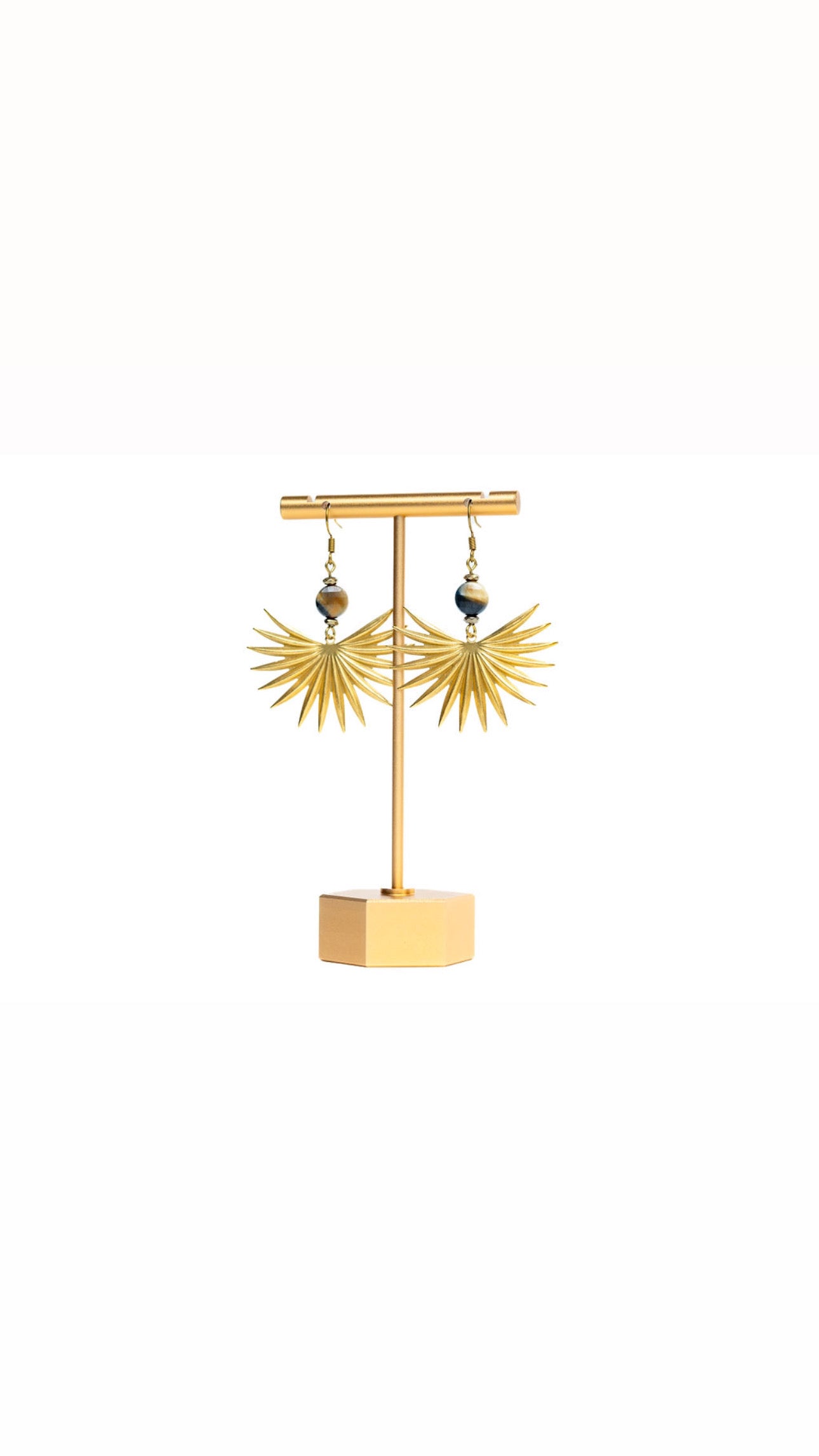 A pair of earrings featuring brass sun spikes and tiger eye coin beads displayed on a gold-colored stand against white background.