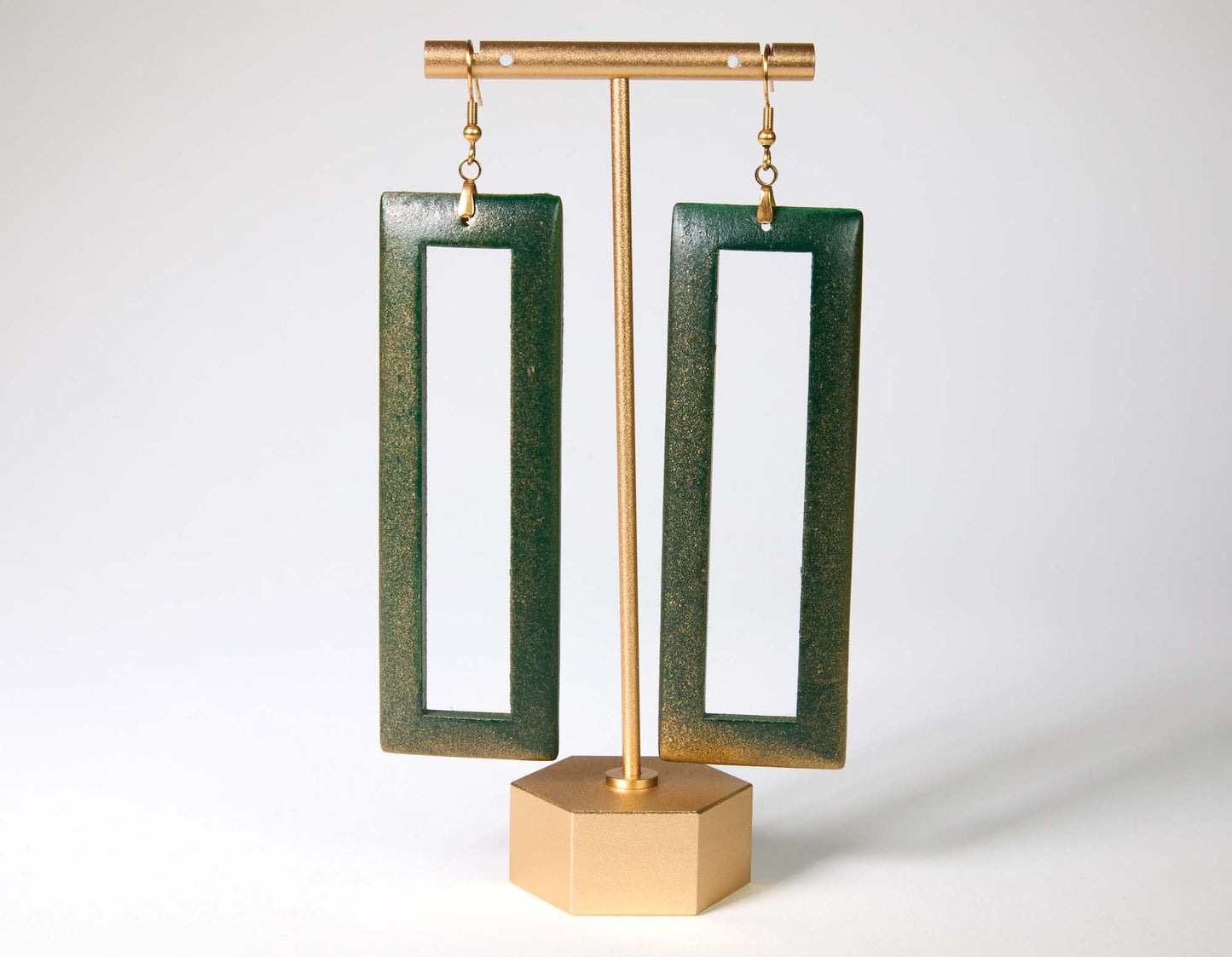Green open rectangular earrings on a gold stand against a white background