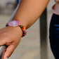 Person wearing a colorful beaded bracelet with a pink stone on a blurred background