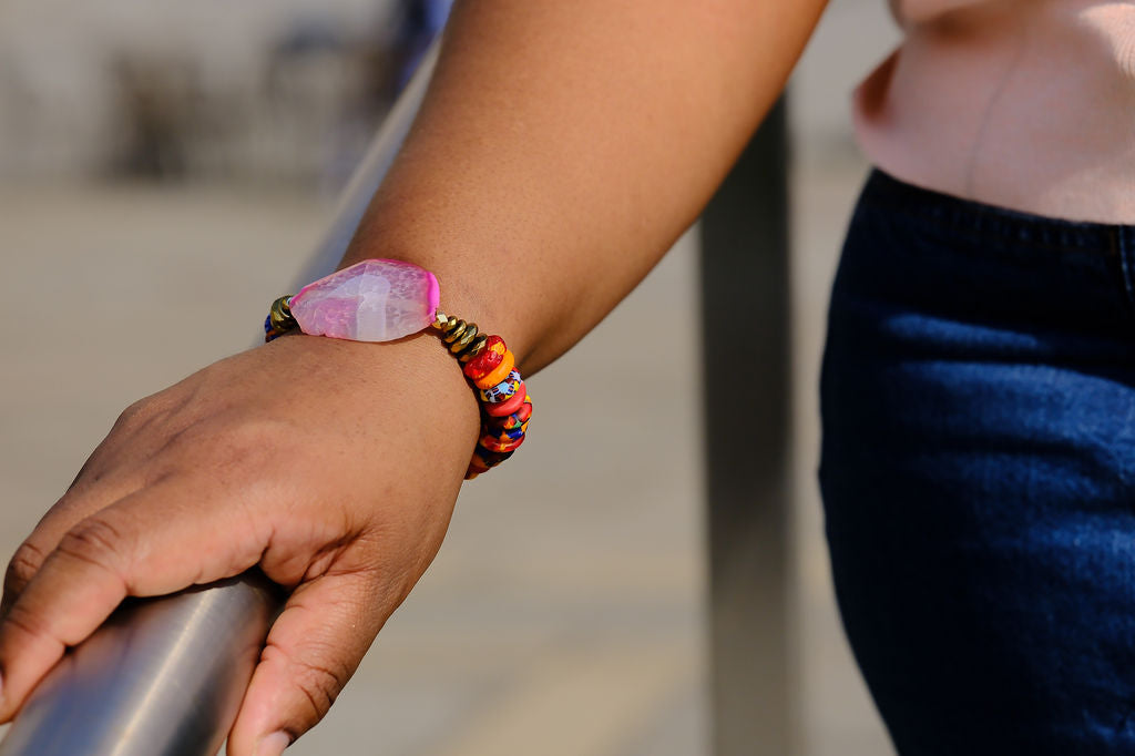 Person wearing a colorful beaded bracelet with a pink stone on a blurred background