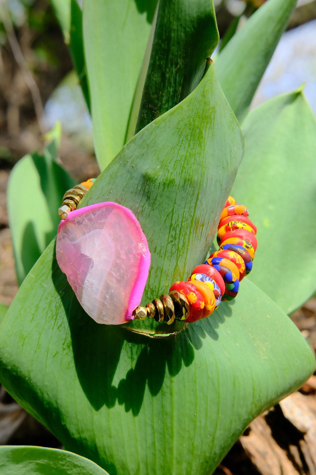 Colorful beaded bracelet with a pink stone on a green leaf