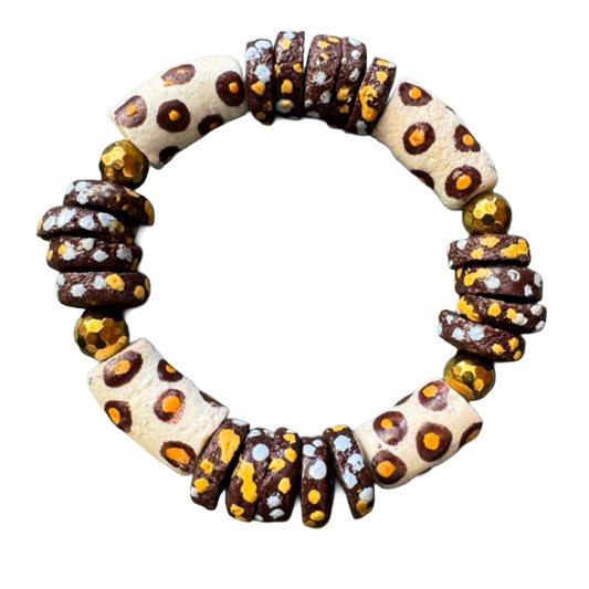 A handmade beaded bracelet featuring alternating cylindrical cream beads with brown and orange leopard spots and faceted dark brown beads with orange and light blue speckles, isolated on a white background.