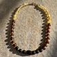 A beaded necklace made of translucent yellow beads, dark brown beads, matte black beads, and a central dark brown textured bead, displayed on a textured stone surface.