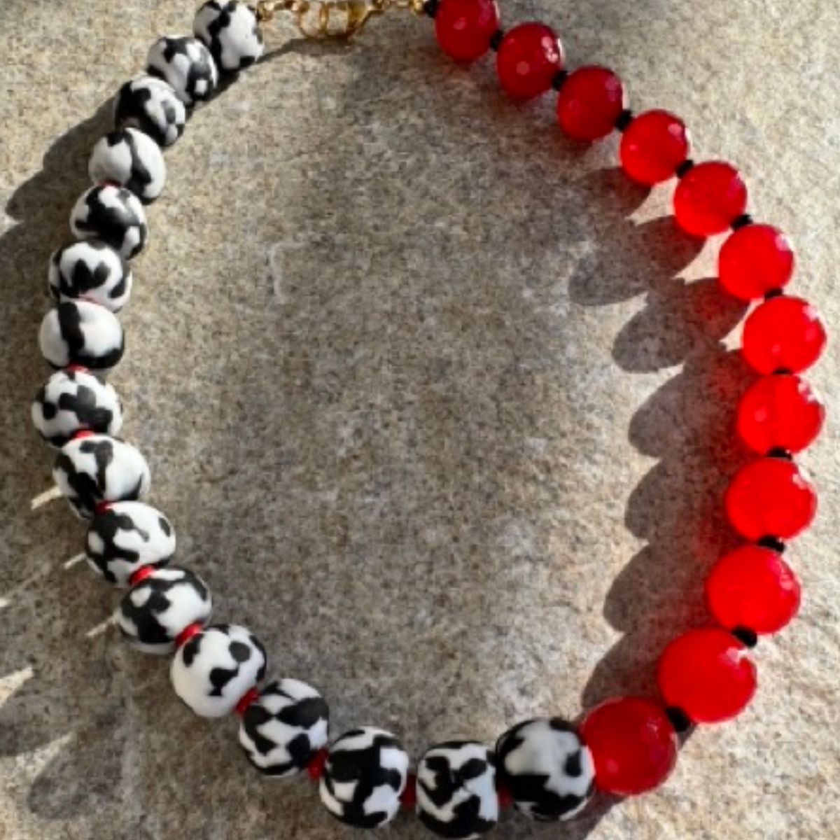 A beaded necklace with alternating red translucent beads and black-and-white mottled beads, displayed on a textured stone surface.