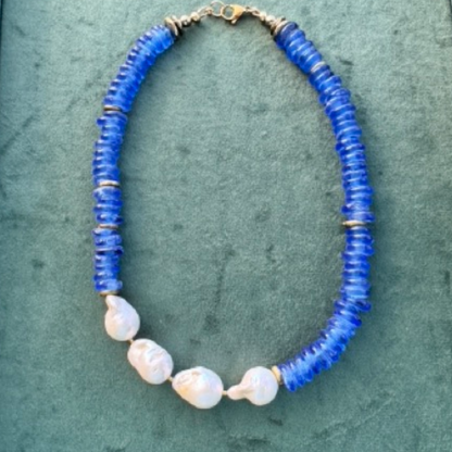 A beaded necklace featuring vibrant blue disc-shaped beads and four irregular white baroque shell beads, displayed on a textured green surface.