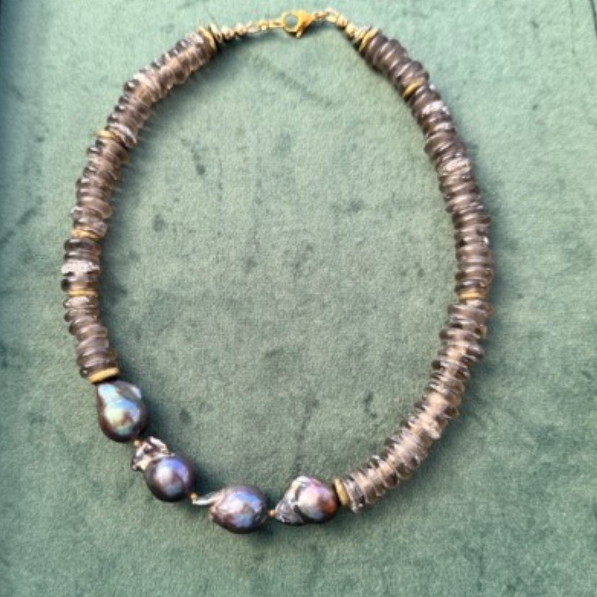 A beaded necklace featuring textured brown disc beads and four large, iridescent baroque pearls, accented with small gold spacers, displayed on a textured green background.