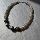 A beaded necklace made of translucent smoky gray beads with four dark iridescent pearls, displayed on a textured gray surface.