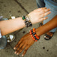 Two people wearing colorful beaded bracelets on a sidewalk.