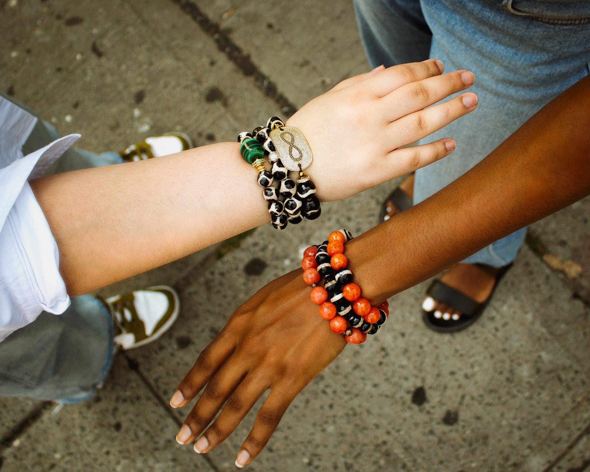 Two people wearing colorful beaded bracelets on a sidewalk.