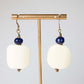 Pair of earrings with white curved edge square beads and blue beads on a gold stand against a light gray background