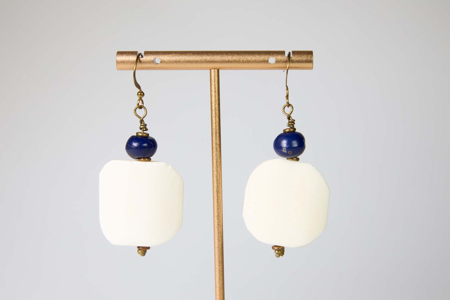 Pair of earrings with white curved edge square beads and blue beads on a gold stand against a light gray background
