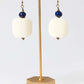 Pair of earrings with white stones and blue beads on a gold stand against a light gray background