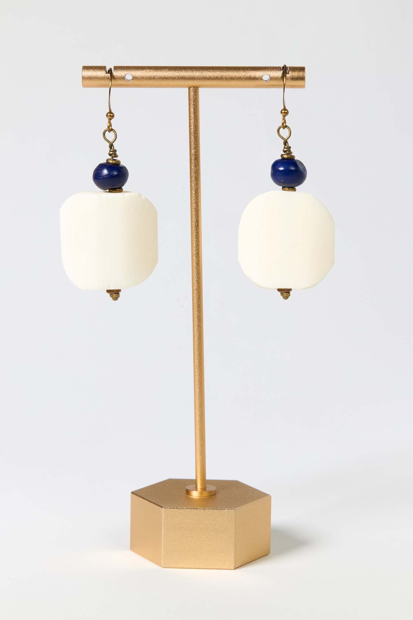 Pair of earrings with white stones and blue beads on a gold stand against a light gray background