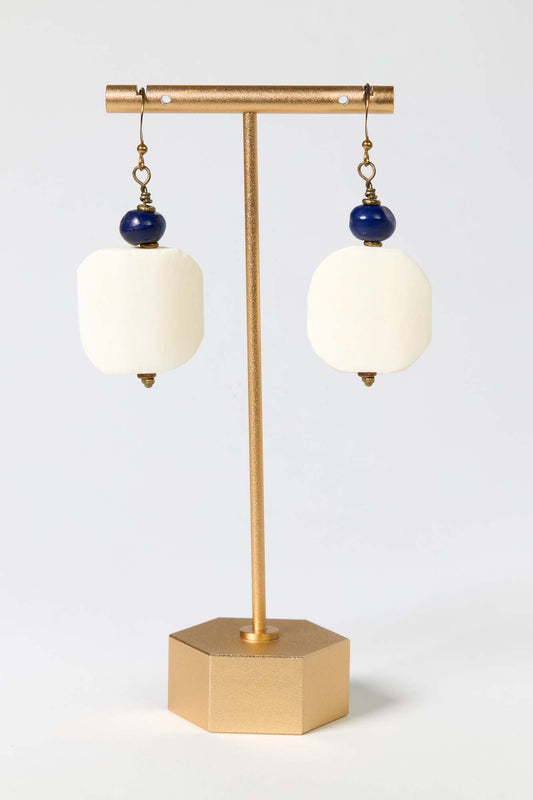 Pair of earrings with white stones and blue beads on a gold stand against a light gray background