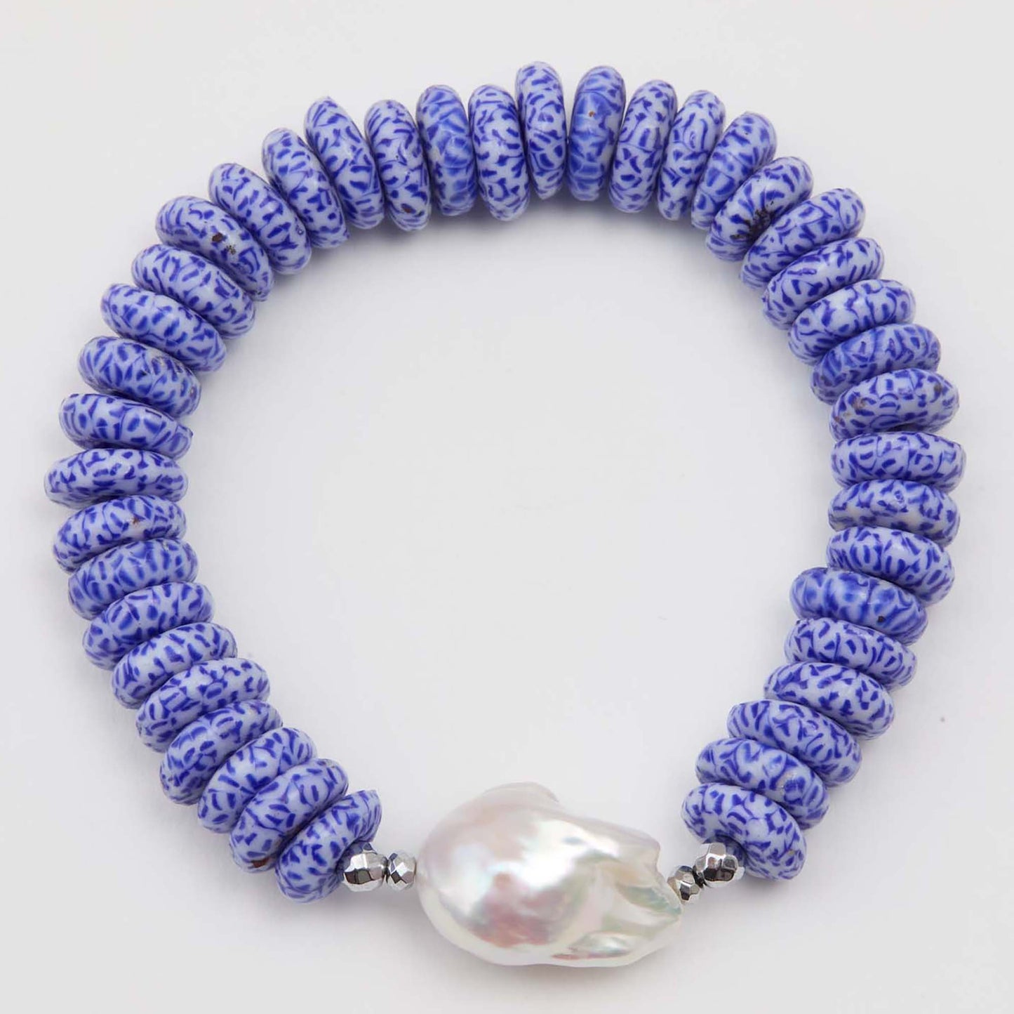 Bracelet with blue and white patterned beads and a large pearl on a white background