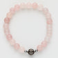 Pink beaded bracelet with a silver and black charm on a white background