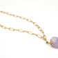 Gold chain necklace with a purple crystal pendant on a white background