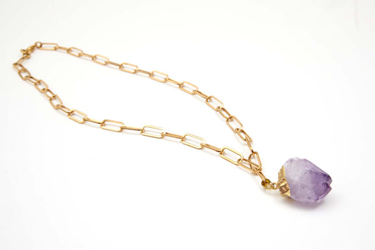 Gold chain necklace with a purple crystal pendant on a white background
