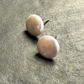 Two round pearl stud earrings with gold posts, resting on a textured gray surface.