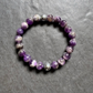 A beaded stretch bracelet made of polished purple and white marbled gemstone beads, displayed on a textured gray slate surface.