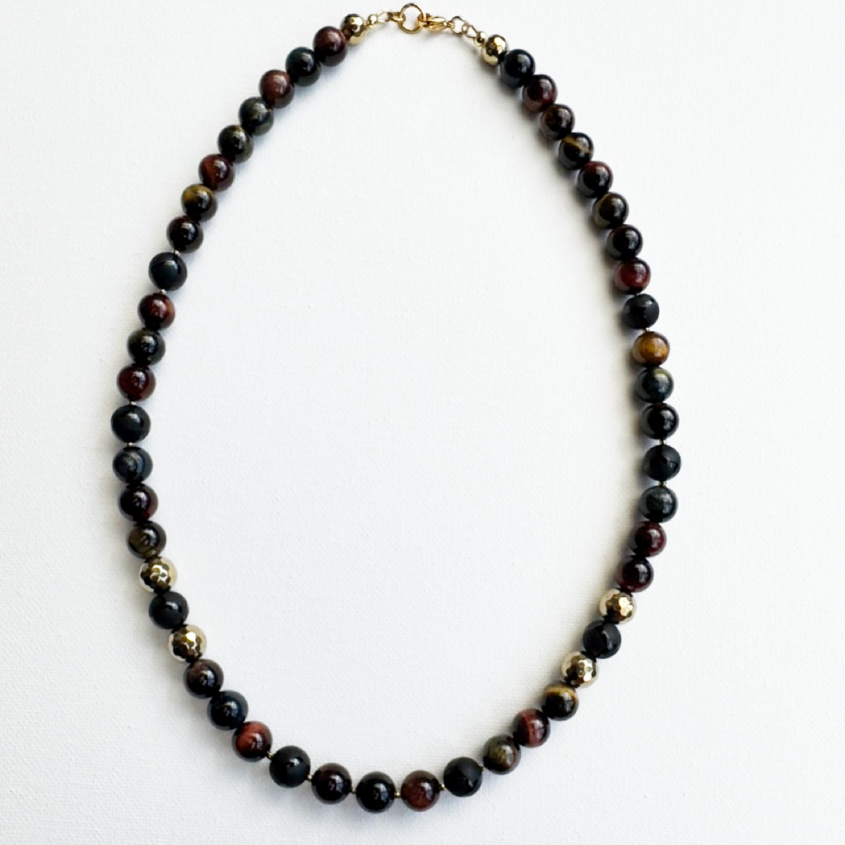 A beaded necklace made of polished round dark brown and black gemstone beads with small metallic gold spacer beads and a gold clasp, displayed on a clean white background.