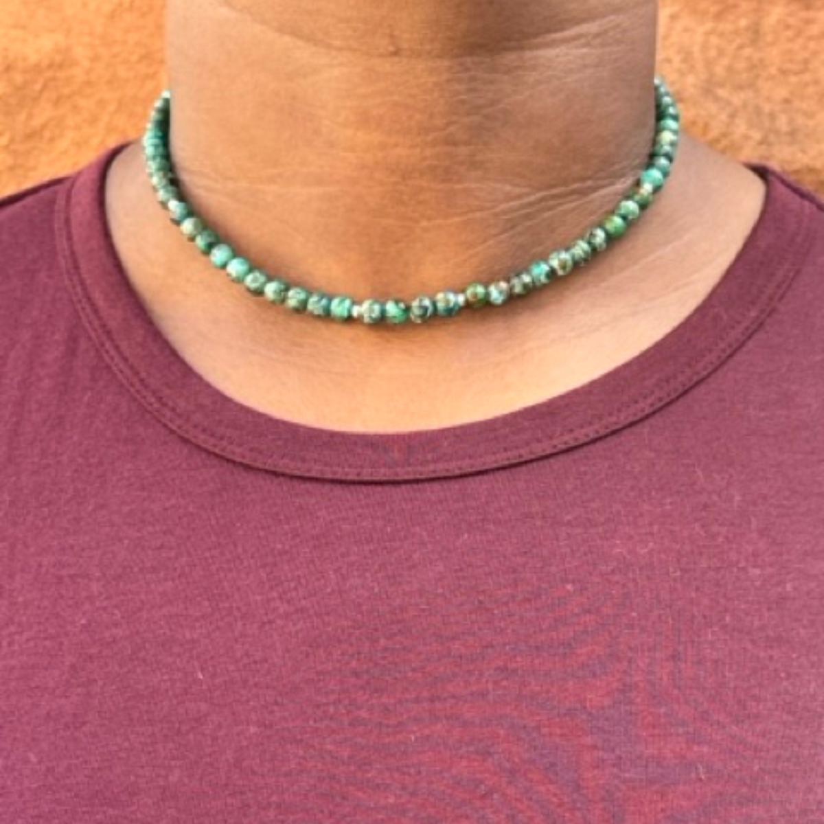 A close-up of a person wearing a beaded choker necklace made of small green marbled beads, paired with a maroon crewneck t-shirt.