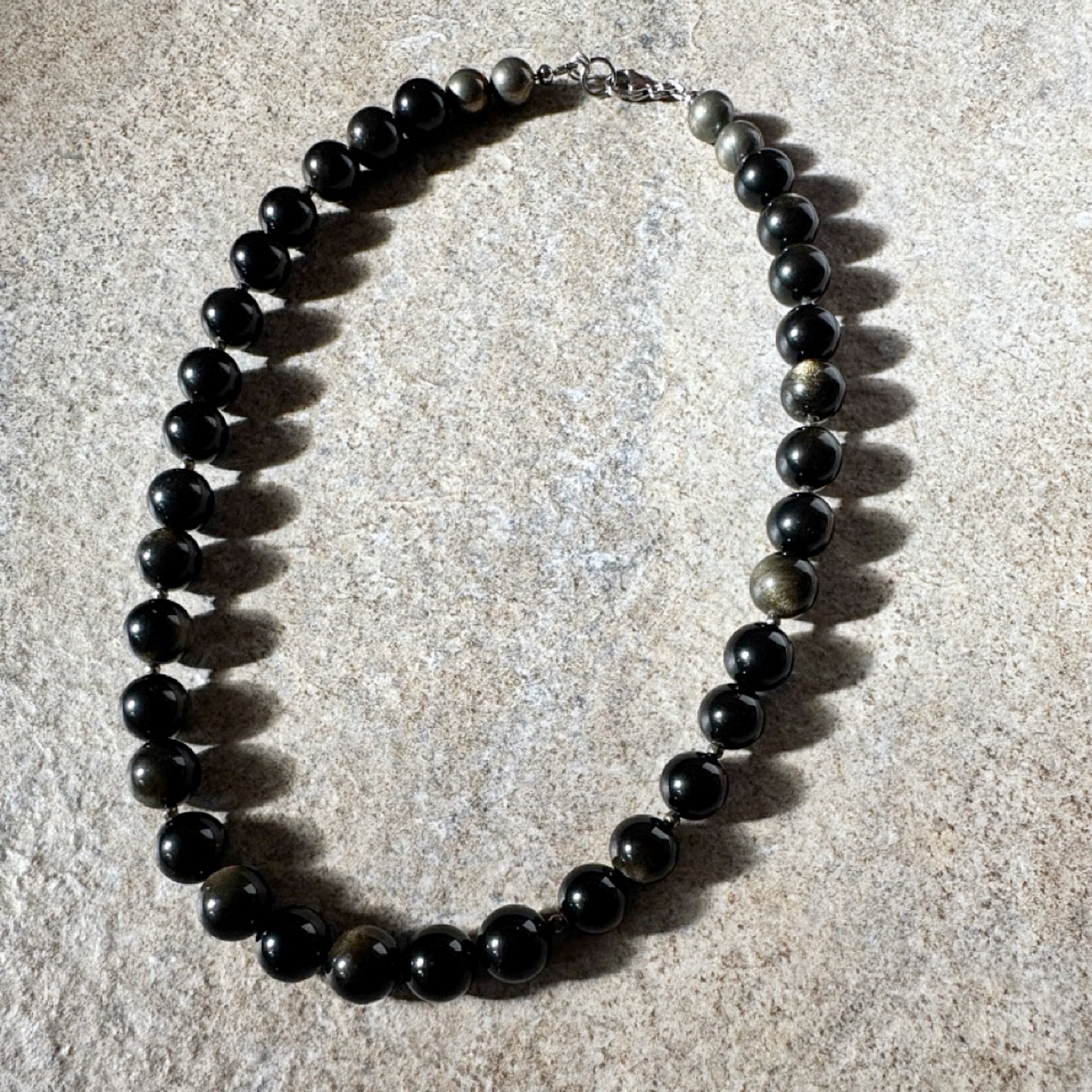 A beaded necklace made of glossy black round beads with a few natural stone accents, displayed on a textured light beige surface.