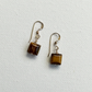 A pair of dangling earrings with square brown tiger's eye stones and gold-toned fishhook wires, displayed on a textured white background.