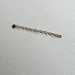 A delicate gold chain extender with a small round  pendant, laid flat on a textured white fabric background.