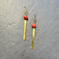A pair of gold-toned dangle earrings with faceted red beads and long rectangular gold bars, displayed on a textured gray background.