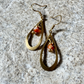 A pair of gold-toned teardrop dangle earrings with small orange and white marbled bead accents, displayed on a textured gray stone surface.