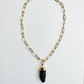 A gold paperclip chain necklace with a polished black crystal pendant, displayed against a clean white background.