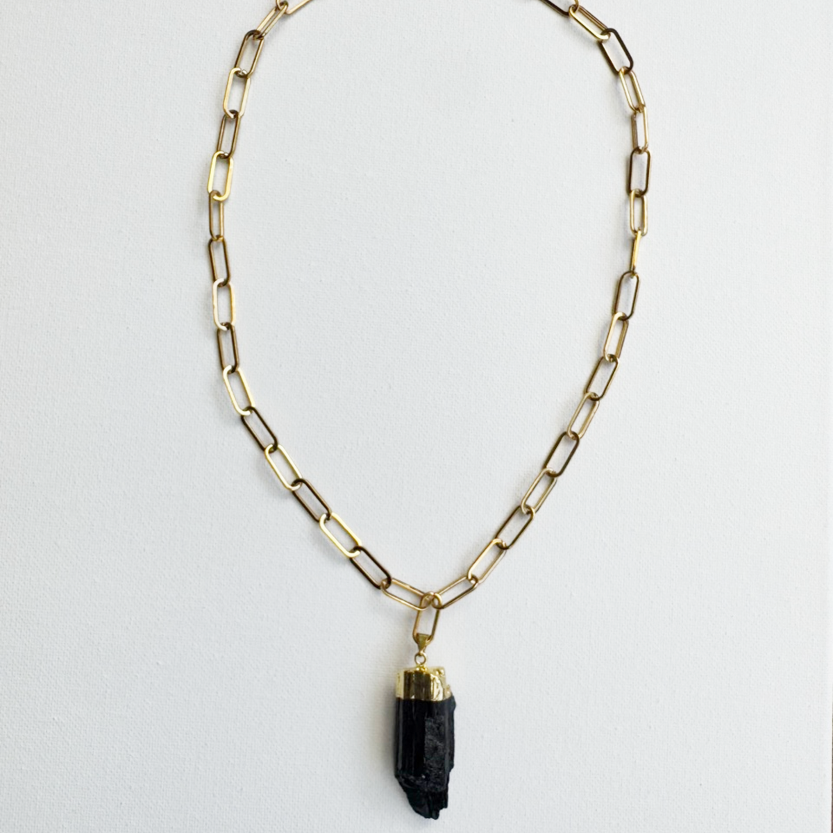 A gold paperclip chain necklace with a polished black crystal pendant, displayed against a clean white background.