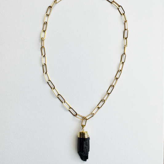 A gold paperclip chain necklace with a polished black crystal pendant, displayed against a clean white background.