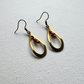 A pair of gold-toned teardrop dangle earrings with small red and gold beads, displayed on a textured white fabric background.