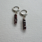 A pair of silver hoop earrings with dangling vertical strands of faceted dark red beads, displayed on a textured white fabric background.