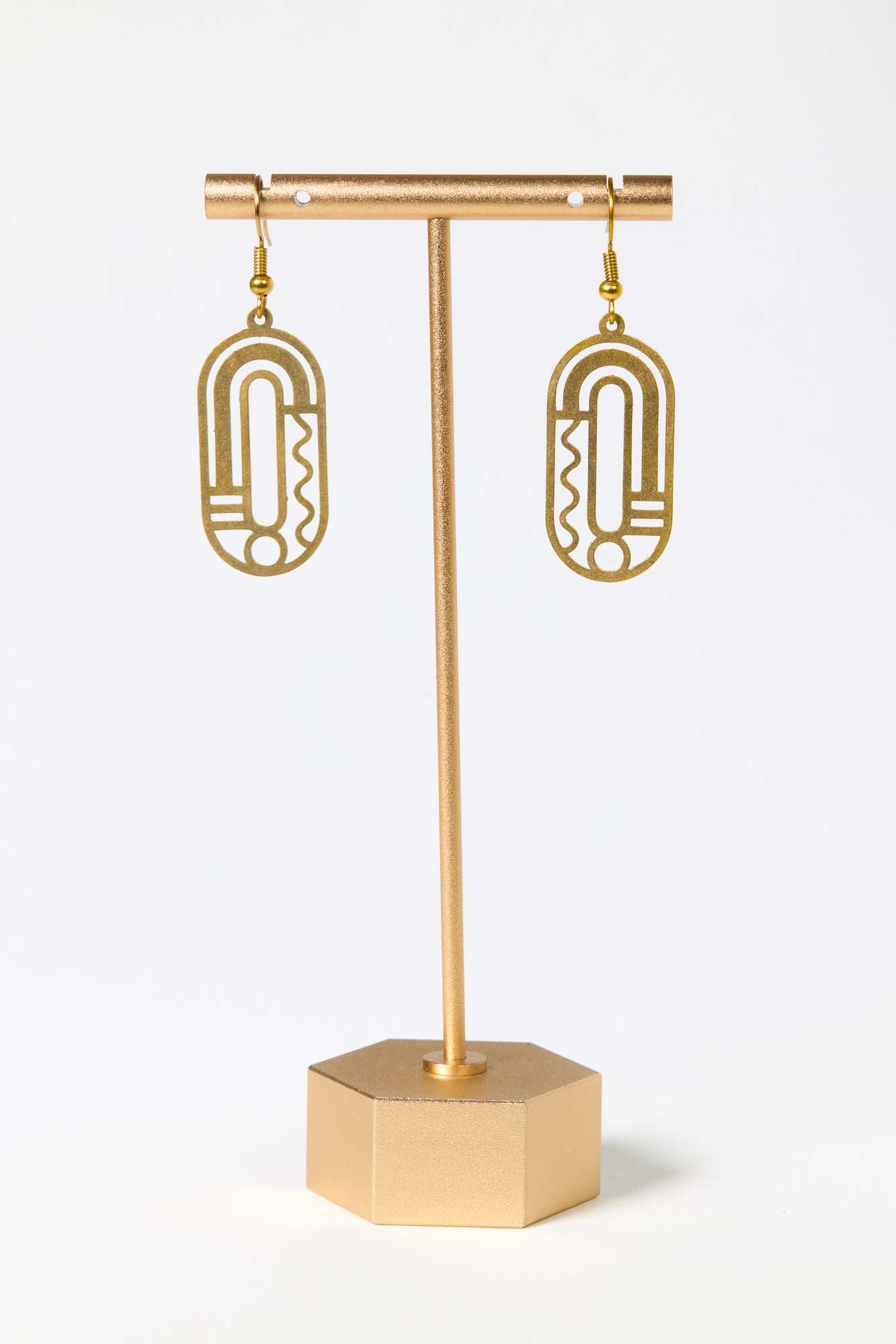 Gold earrings on a matching gold stand against a white background