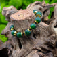 Hunter green bracelet with brass and black accent beads on tree stump against blurred green background