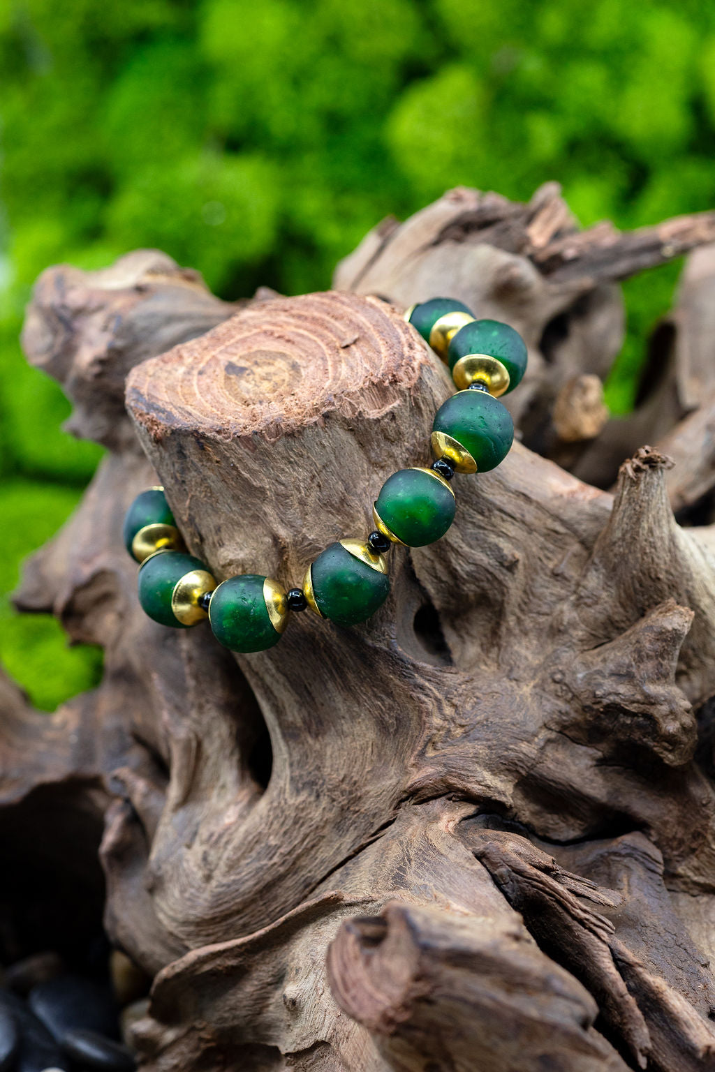 Hunter green bracelet with brass and black accent beads on tree stump against blurred green background