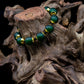 Hunter green bracelet with brass and black accent beads on tree trunk against black background