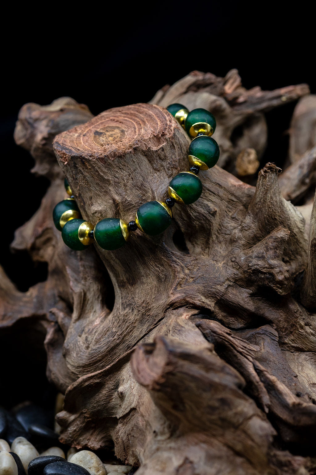 Hunter green bracelet with brass and black accent beads on tree trunk against black background