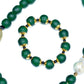 A hunter green beaded necklace with a brass focal bead and a baroque pearl, featuring hematite spacers and lampwork glass beads with matching bracelet against white background.