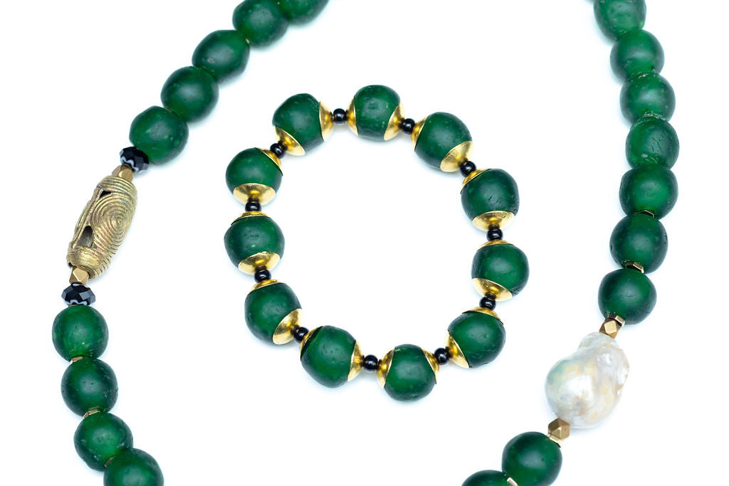 A hunter green beaded necklace with a brass focal bead and a baroque pearl, featuring hematite spacers and lampwork glass beads with matching bracelet against white background.